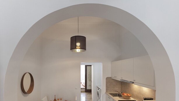 Cozinha moderna com teto arredondado, área de jantar com mesa e cadeiras de madeira, e luminária pendente.