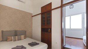 Quarto com cama, guarda-roupa de madeira e banheiro visível por uma porta aberta.
