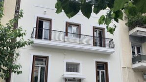 Um edifício de dois andares com varanda, janelas com persianas de madeira e uma porta com portão de metal.