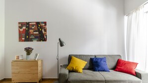 A living room with a grey sofa, wooden side table, floor lamp, and a colorful abstract painting on the wall. - AthanasiouDiakou5 - Colourful apartment under the (Athens)
