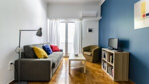 Una sala de estar moderna con un sofá gris, una mesa de centro blanca, una estantería y un televisor.