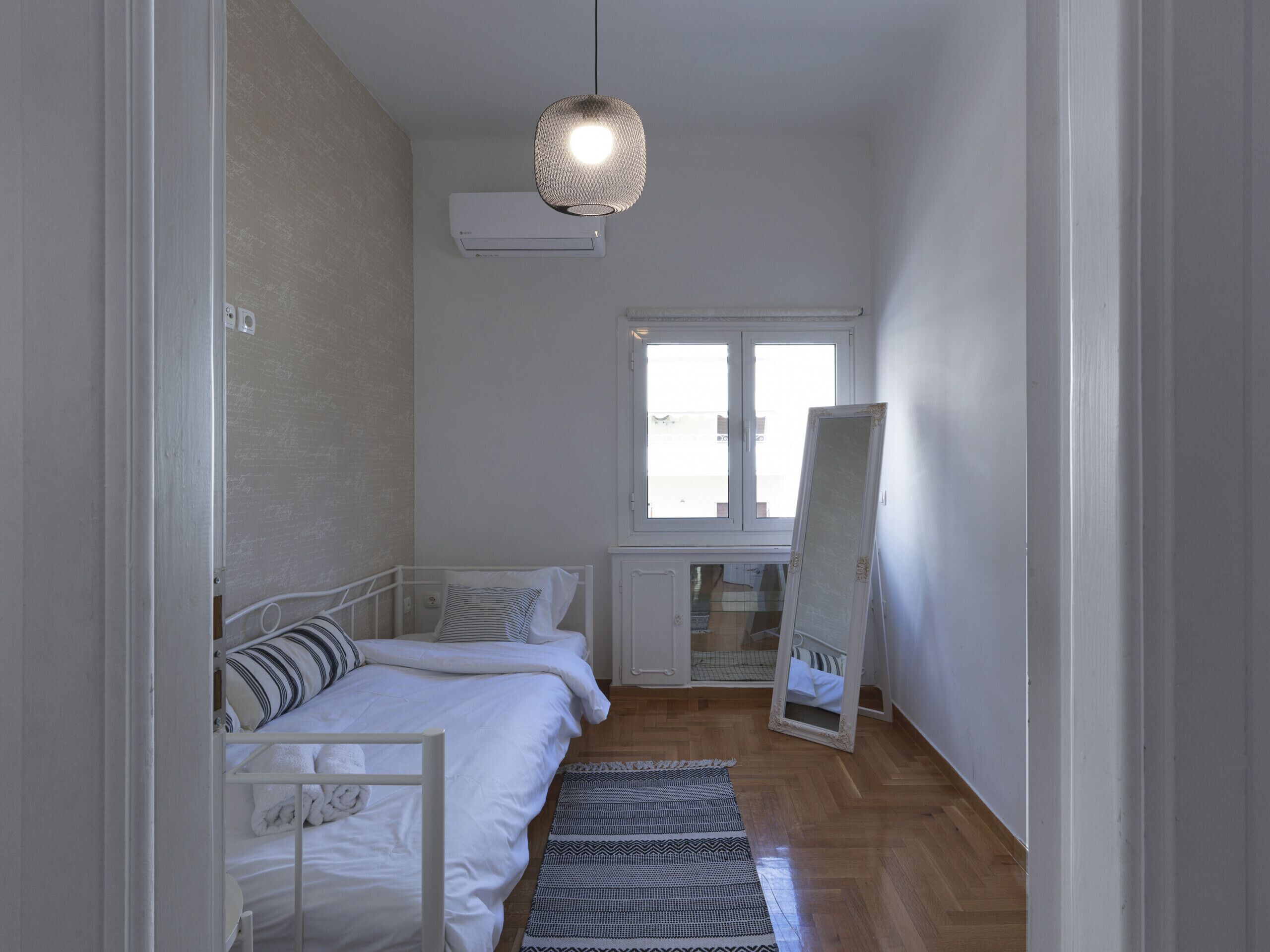 A bedroom with a bed, a hanging light fixture, a window, and a radiator.
