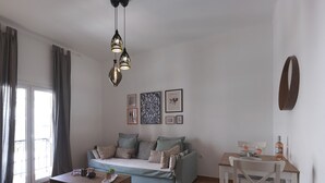 Ett modernt vardagsrum med en soffa, ett soffbord och en matplats. Det finns gardiner, konst på väggen och en taklampa.
