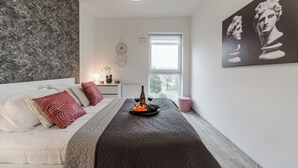 A modern bedroom with a bed, a bedside table, a window, and a wall with a painting. - Lumina apart near Cinema Museum (Lodz)