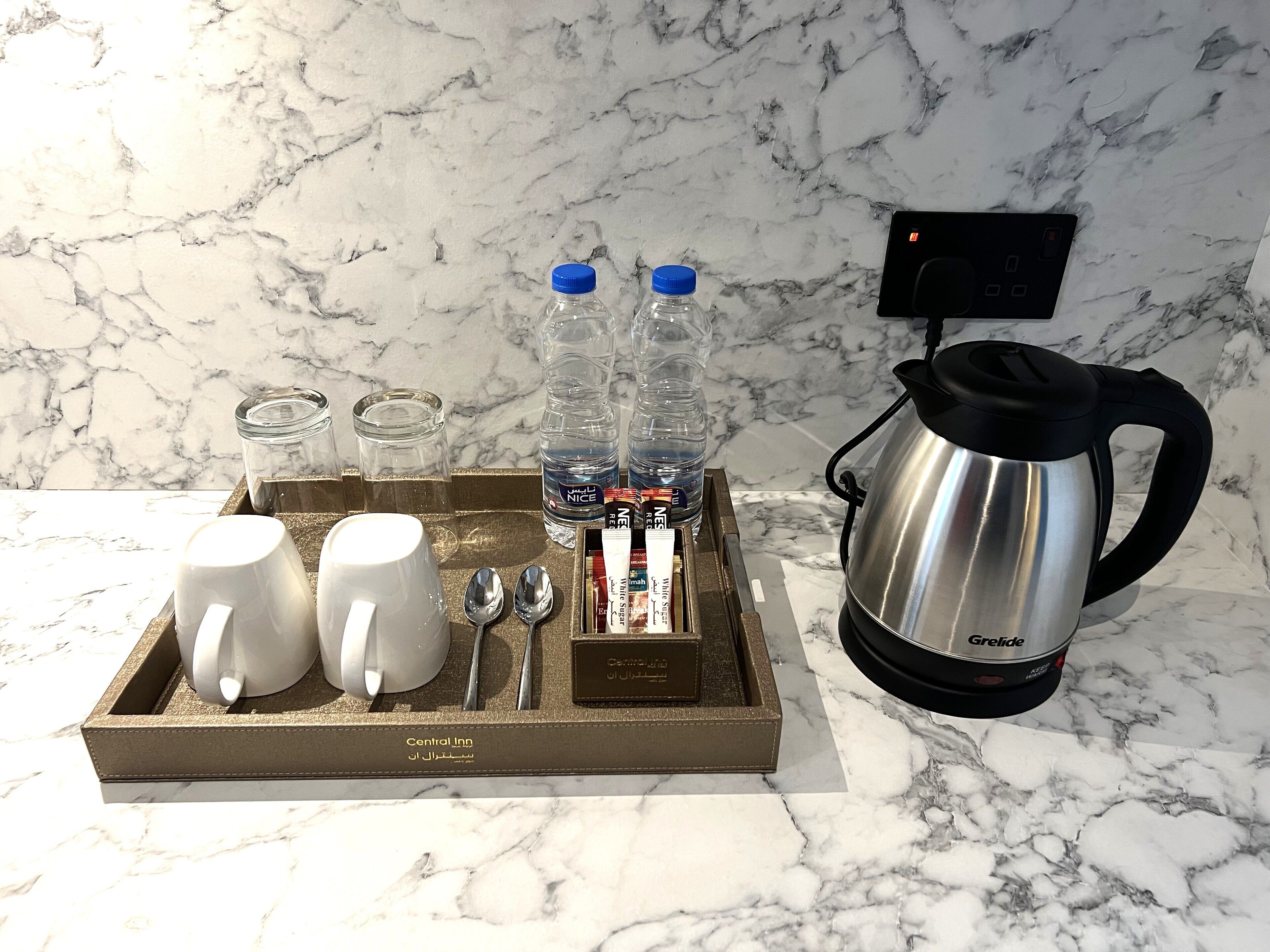 Un plateau contenant une cafetière, des bouteilles d’eau, des verres et une boîte étiquetée « Central Inn ».