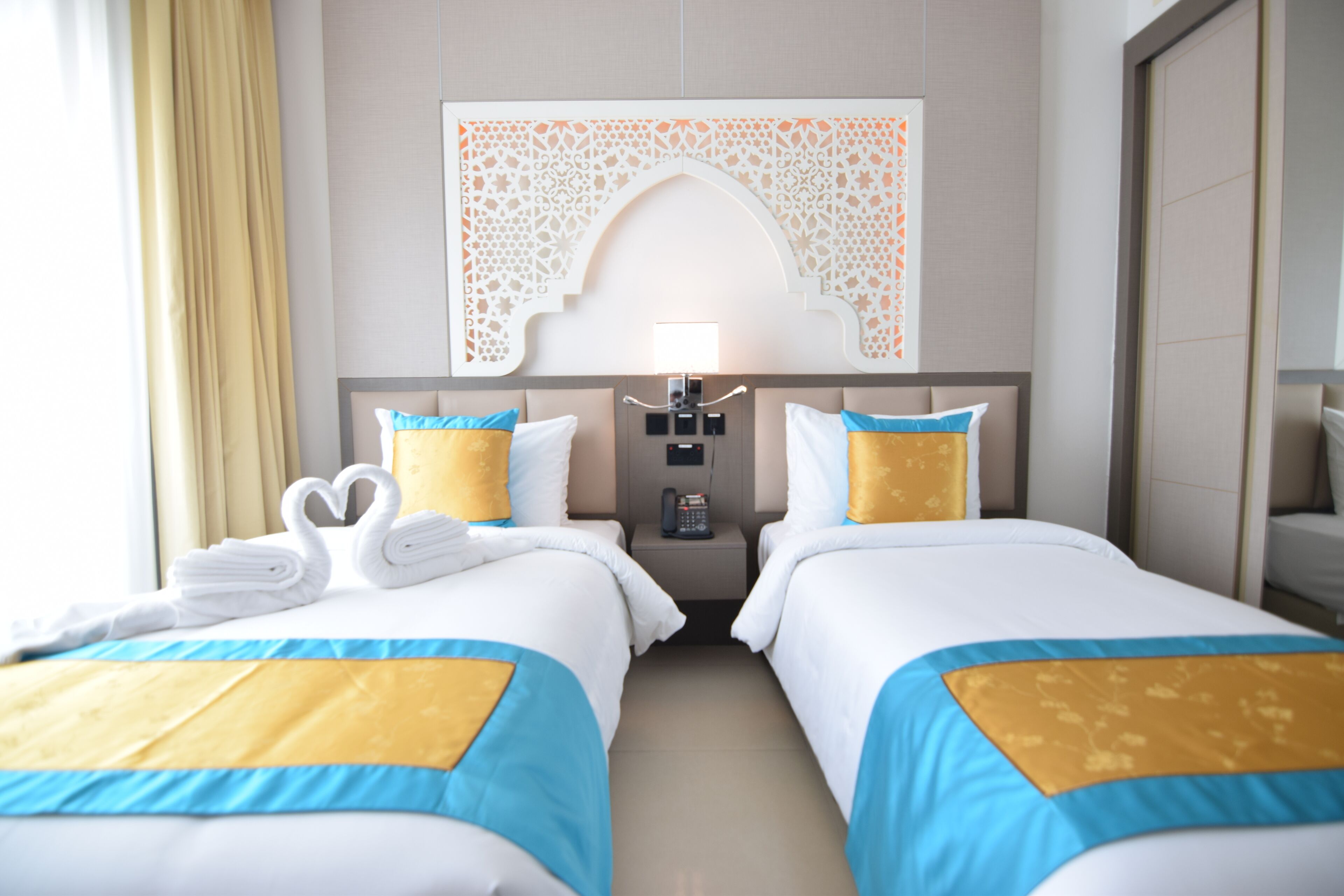 Habitación de hotel con dos camas, un panel decorativo en la pared, un teléfono en la mesita de noche y un espejo.