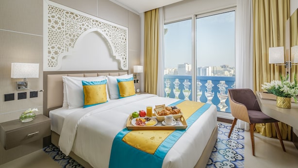 A hotel room with a large bed, breakfast tray, city view, and a balcony with a railing. - Central Inn Souq Waqif (Doha)