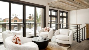 A modern living room with large windows, a wooden ceiling, and a staircase. - Ski-In/Ski-Out | Hot Tub | Game Room (Big Sky)