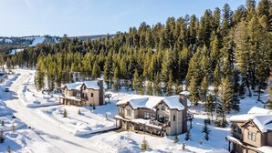A snow-covered lodge with multiple cabins, surrounded by dense forest and a clear sky. - Ski-In/Ski-Out | Hot Tub | Game Room (Big Sky)