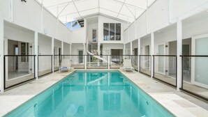 A large indoor swimming pool with glass railings, a central staircase, and a modern architectural design.