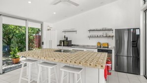 A modern kitchen with a large island, stainless steel appliances, and a sliding glass door leading to a garden.