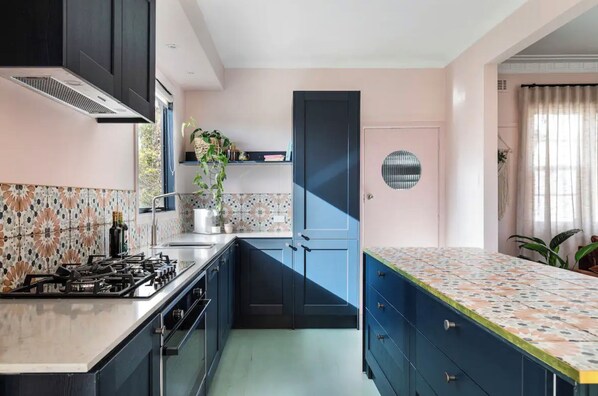Compact kitchen with a gas stove, sink, and patterned backsplash, complemented by dark cabinetry and a blue door.