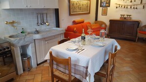 A dining area with a table set for four, a kitchen with a sink and stove, and a living area with a sofa and a painting on the wall. - La Campanelle (Montemezzo)