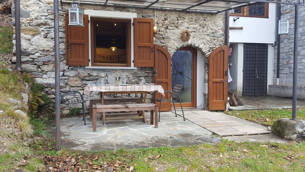 A stone building with wooden doors and windows, a table with chairs, and a small outdoor seating area. - La Campanelle (Montemezzo)