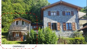 A stone house with a wooden porch and shutters, surrounded by greenery. - La Campanelle (Montemezzo)