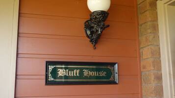 Uma placa com a inscrição 'Bluff House' fixada numa parede com linhas horizontais e um candeeiro decorativo acima.