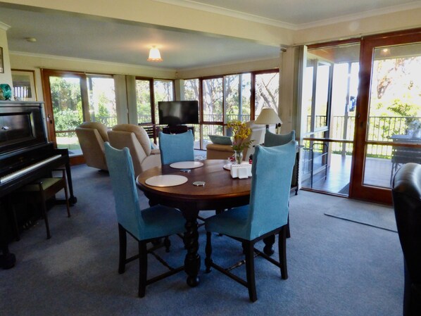 A dining area with a round table, chairs, a piano, and a television.