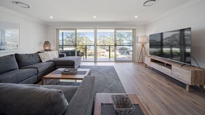 A modern living room with a sectional sofa, a coffee table, a TV on a wooden stand, and large windows with a view.