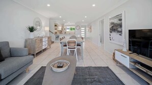 A modern living room with a sofa, coffee table, TV, and a dining area with chairs and a table.