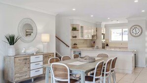 A modern kitchen with white cabinetry, a central island, and a dining area with wicker chairs.