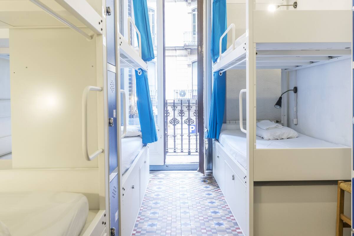 A narrow corridor with bunk beds on either side, a tiled floor, and a view through a barred window.