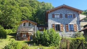 Ein Haus aus Stein mit Holzhörnern und einem kleinen Anbau, umgeben von üppigem Grün.
