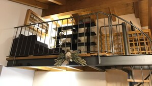 Eine Holztreppe mit Metallgeländern führt zu einer Erkerzone mit Regalen und einem dekorativen Kranz.
