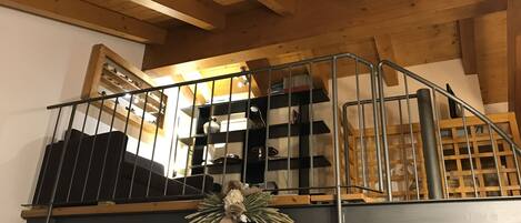A wooden staircase with metal railings leading to a loft area with shelves and a decorative wreath.