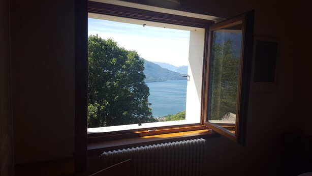 Ein Zimmer mit großem Fenster mit Blick auf einen See und Berge.