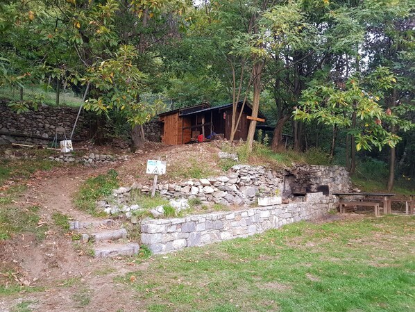 A rustic cabin with a stone foundation and a wooden structure, surrounded by trees and a stone wall. - Le Papere apartment in Chalet di Cher (Montemezzo)