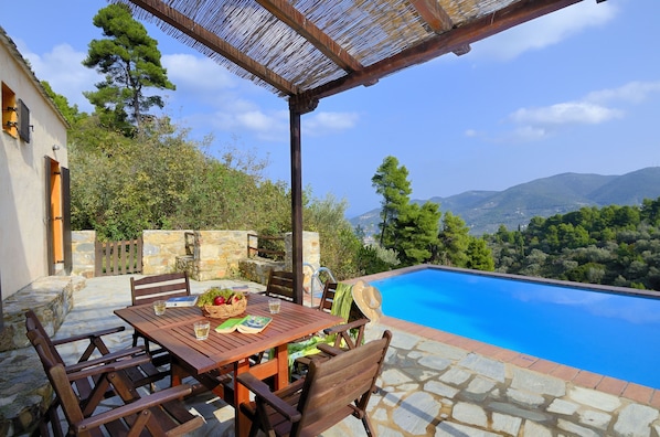 A wooden table with chairs and a poolside view of a mountainous landscape.