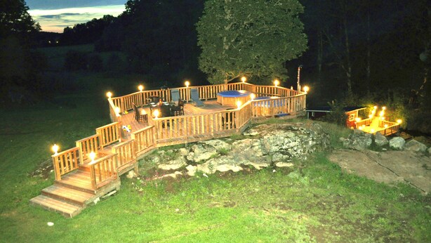 A wooden deck with a railing, a hot tub, and a small table and chairs.