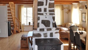 A rustic cabin interior with a stone fireplace, wooden floors, a staircase, and a cozy seating area.