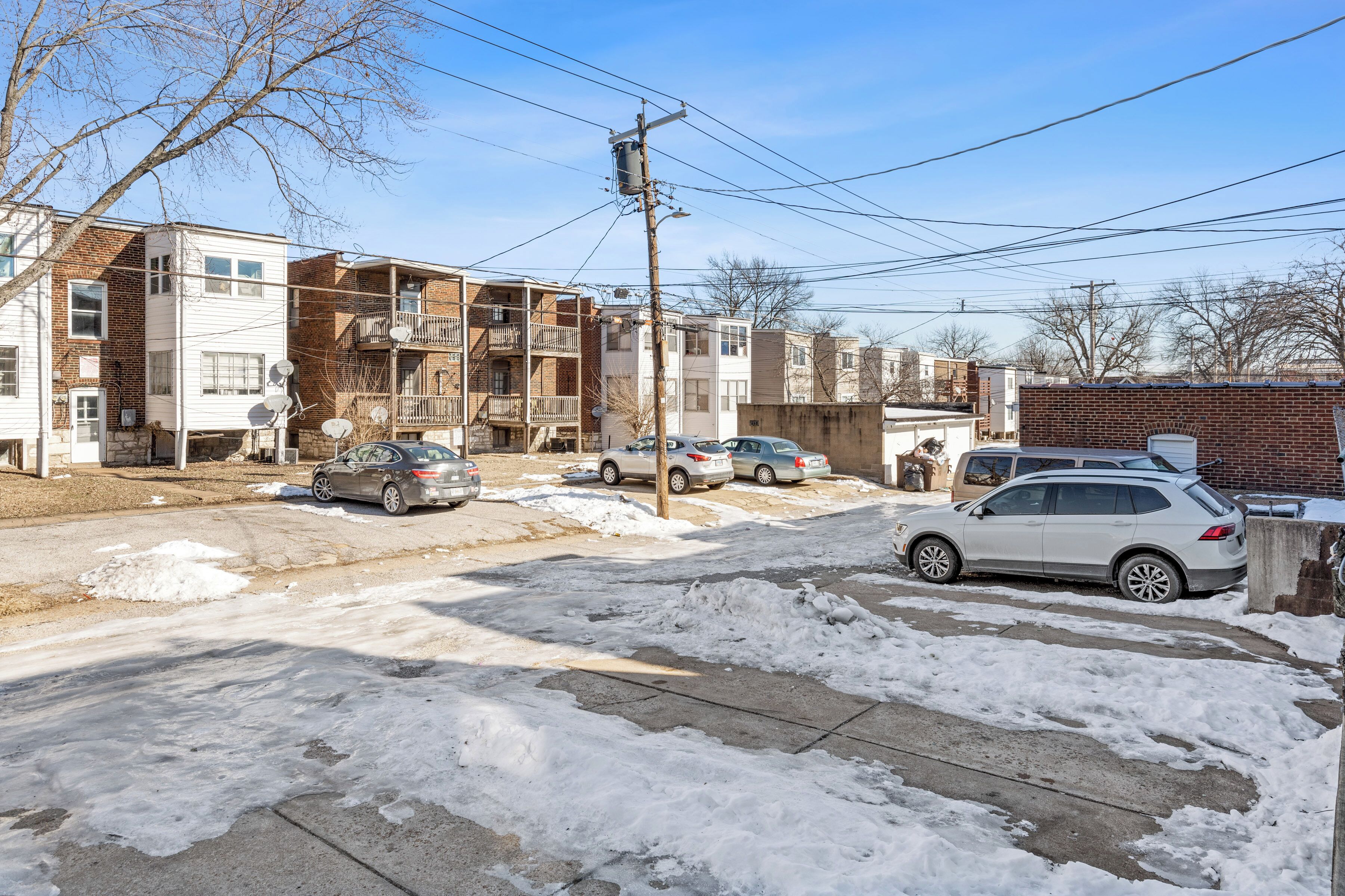 A residential street with multiple two-story apartment buildings, parked cars, and a visible utility pole.