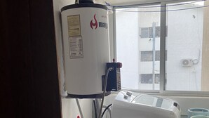 Une pièce équipée d’un chauffe-eau, d’un lave-linge et d’une fenêtre donnant sur des immeubles.