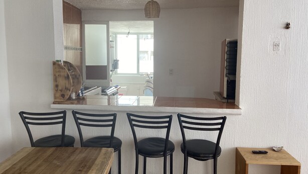 Un coin repas avec une table en bois et quatre chaises noires. On y trouve une petite table d’appoint en bois, sur laquelle reposent une télécommande et un objet décoratif.