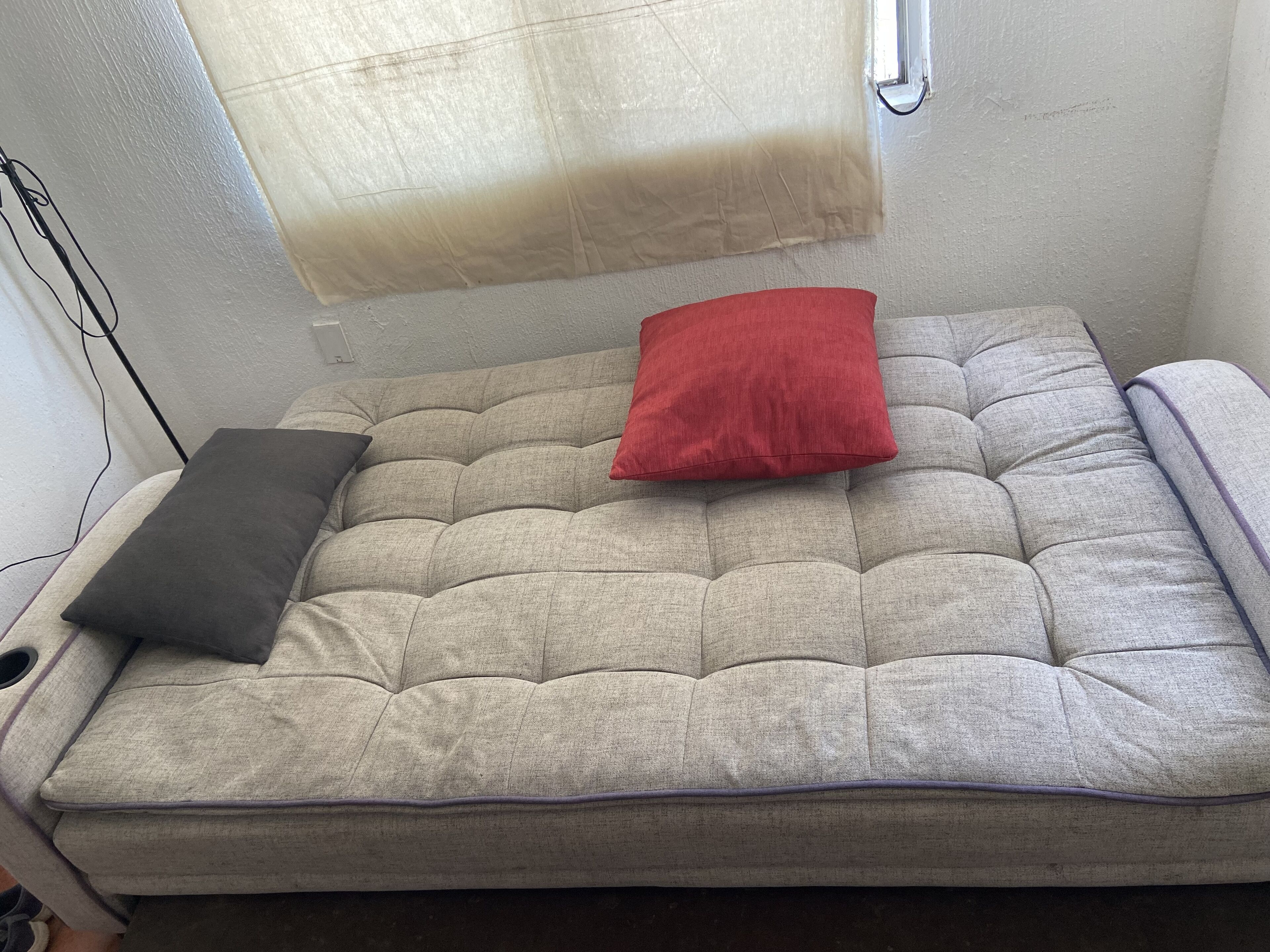 A small, cozy room with a single bed, a window with a curtain, and a wall socket.