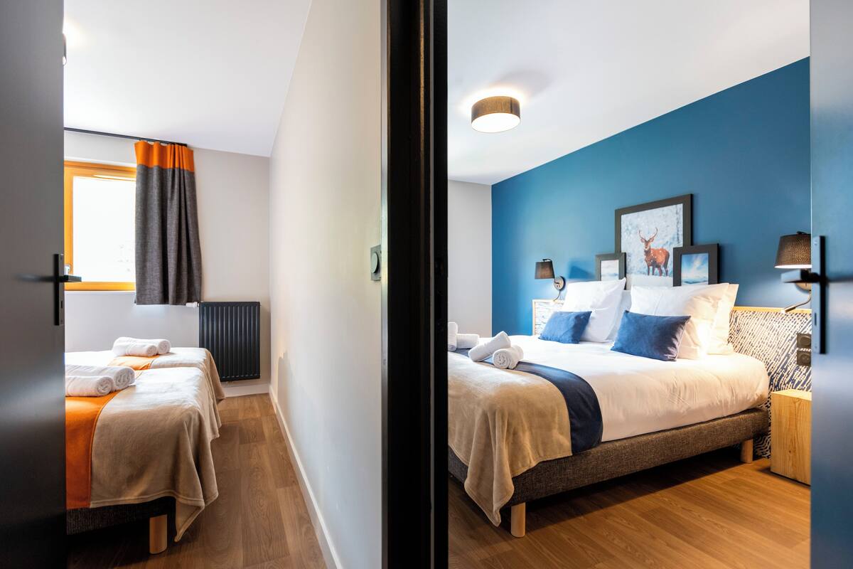 A hotel room with two beds, a blue accent wall, and a window with curtains.