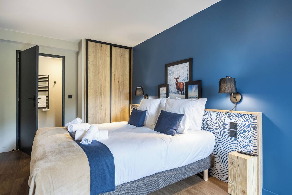 A modern bedroom with a large bed, wooden headboard, and a blue accent wall.