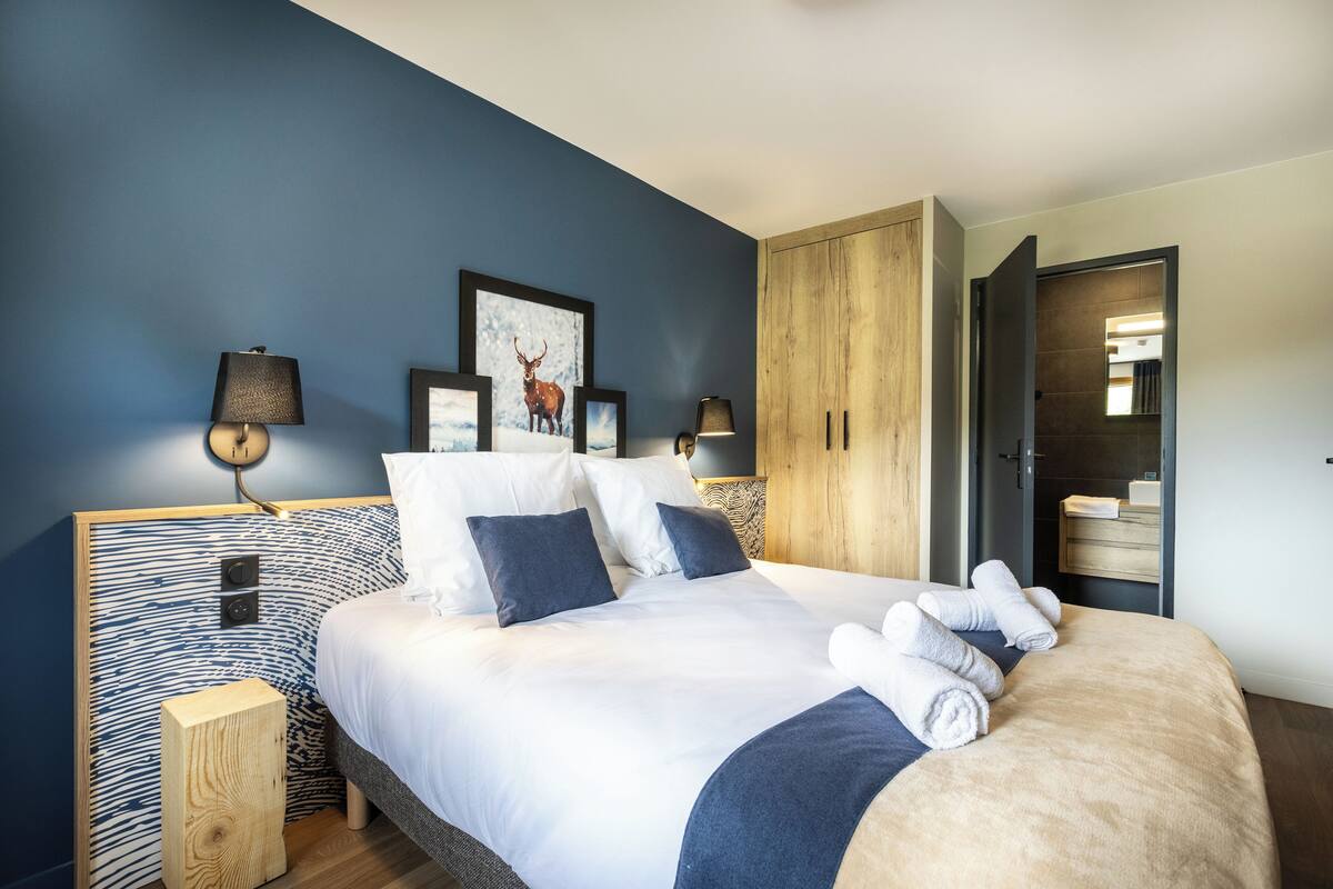 A modern bedroom with a large bed, two bedside tables, a wooden wardrobe, and a framed deer picture on the wall.