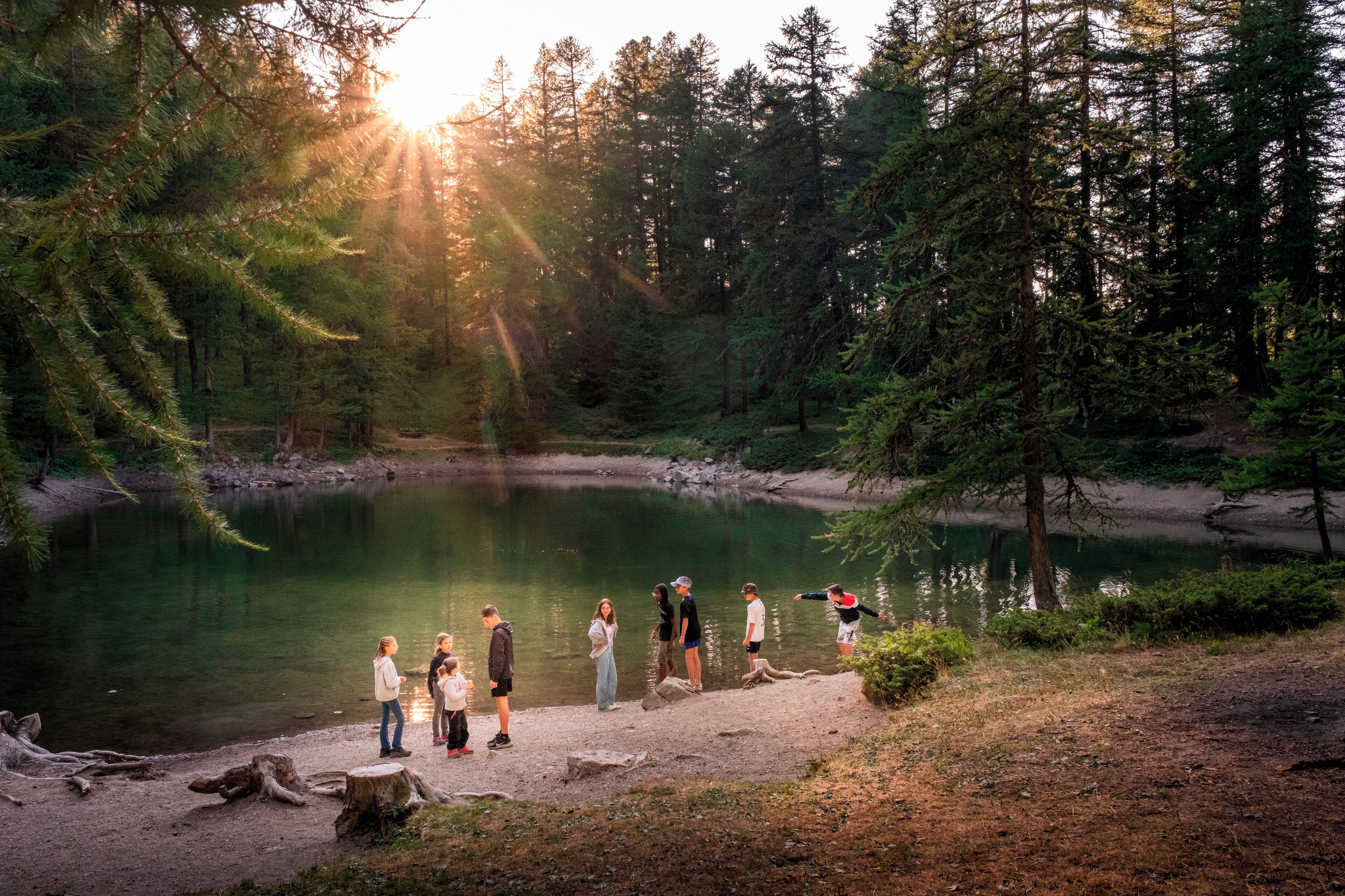 A group of people by a lake surrounded by trees.