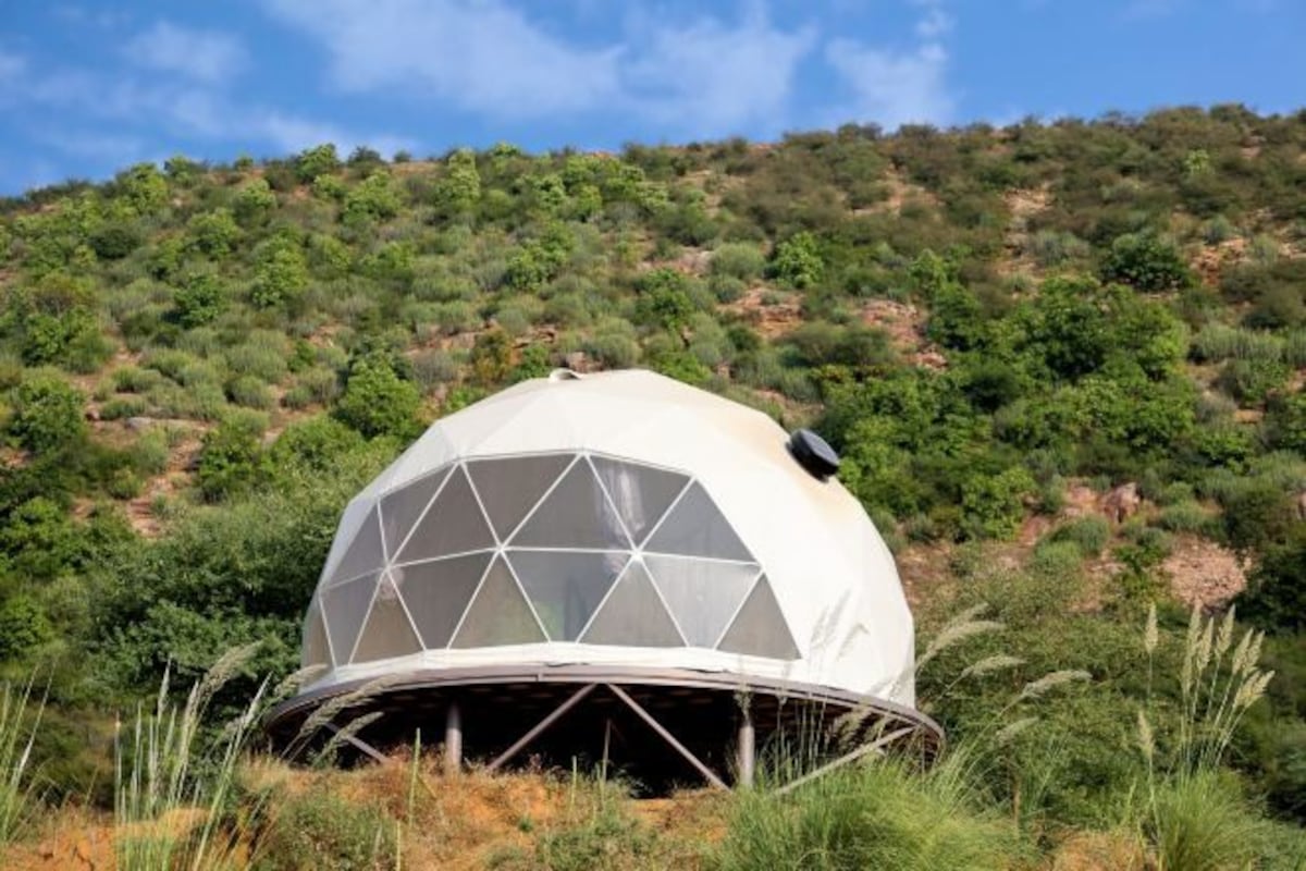 Una struttura a cupola geodetica in un ambiente naturale, con una collina sullo sfondo.