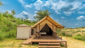 Uma tenda safári com um deck de madeira, uma estrutura pequena anexa e vista para a paisagem ao redor.