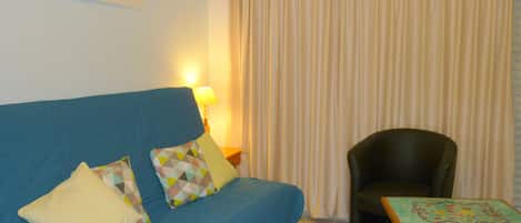 A living room with a blue sofa, a black armchair, a small table, and a painting on the wall.