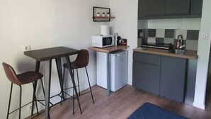 Una cocina compacta con microondas, refrigerador y gabinetes oscuros. Hay una pequeña mesa con dos sillas y un cuadro en la pared.