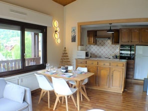 A cozy kitchen with wooden cabinets, a dining table with chairs, and a view of the outdoors through a window. - Duplex with balcony and parking in Samoëns - Ideal for remote work (Samoëns)