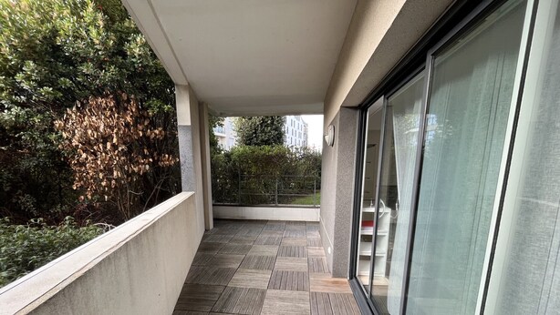 Un balcón moderno con suelo de baldosas, una puerta de cristal y vistas al verdor.