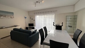 Una sala moderna con sofá, mesa de comedor, sillas, televisor y una vitrina de vidrio.
