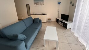 Una sala de estar moderna con un sofá azul, una mesa de centro blanca, un televisor y una mesita auxiliar.