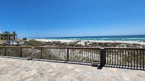 Vista a la playa desde un balcón con suelo de baldosas y barandilla de madera.